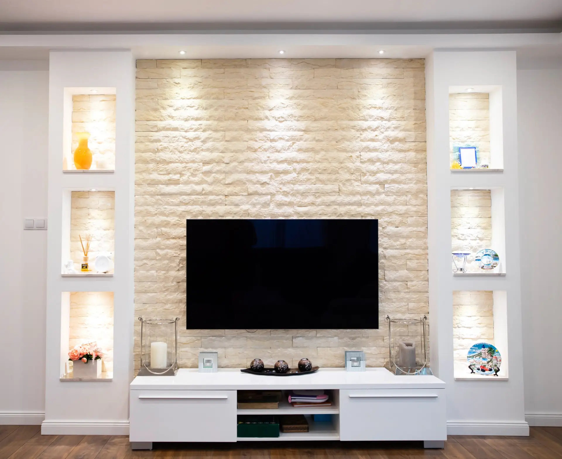 Wall-mounted flat-screen TV installed on a feature stone wall in a modern Adelaide living room, with built-in shelving and accent lighting.